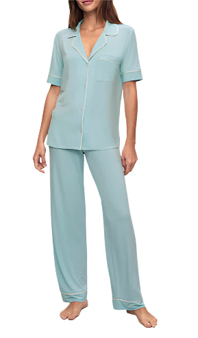 A person is barefoot in the Eberjey Gisele Short Sleeve Long Pant PJ Set by Eberjey, featuring light blue pajamas with a classic-fit top, short-sleeve button-up shirt, and low-rise straight leg pants with an elastic waistband.