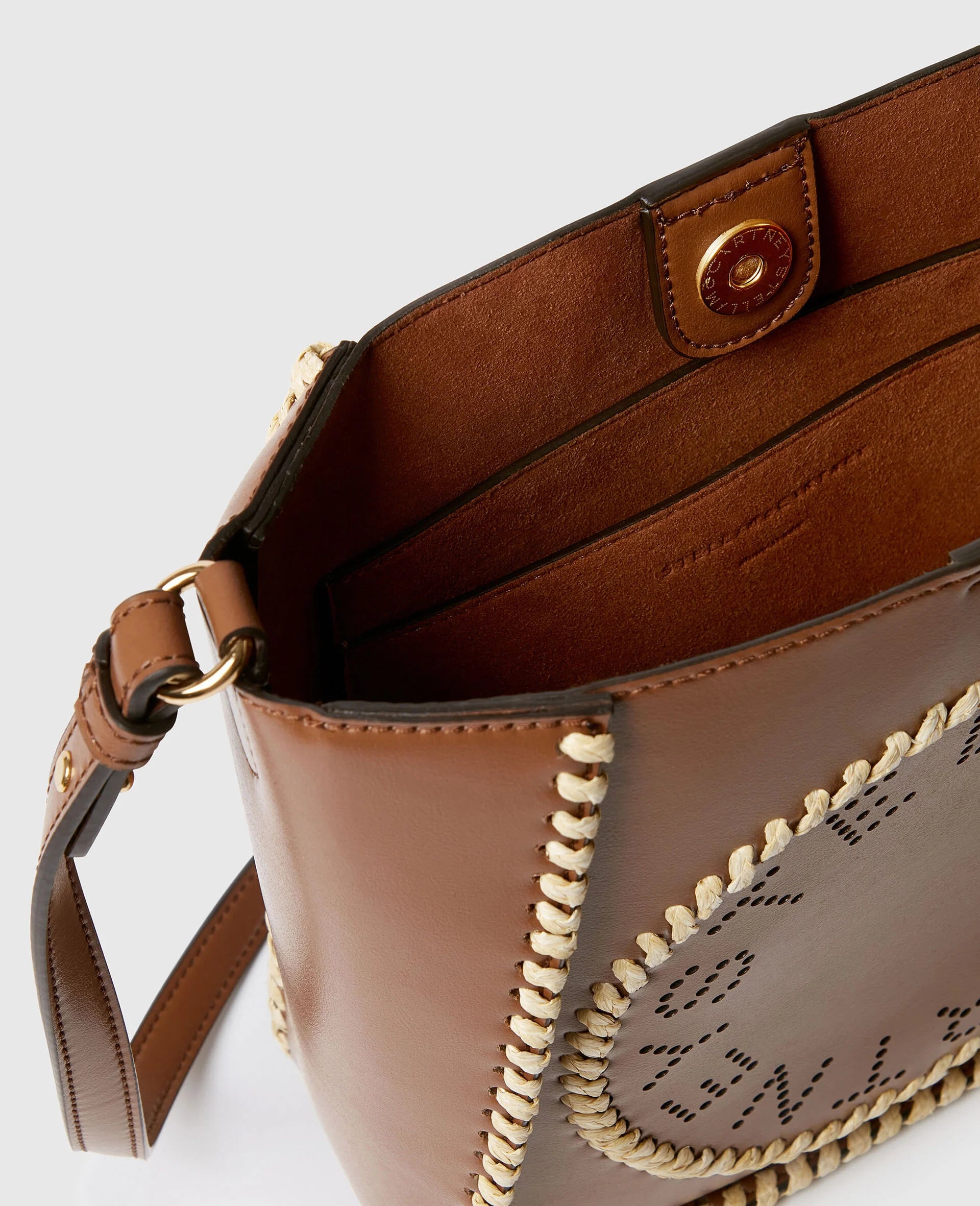 Close-up of the Stella McCartney Logo Raffia Trim Crossbody Bag, featuring brown vegan leather, cream stitching, gold magnetic snap closure, adjustable shoulder strap, and visible interior pockets.