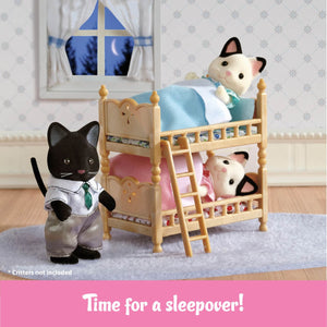 Two Calico Critters figures are cozily tucked into the Stack and Play Beds, each with a soft blanket, while a third cat in a shirt and tie stands close by. A window reveals the night sky, completing this charming dollhouse furniture scene from Calico Critters. The text below reads: “Time for a sleepover!”.