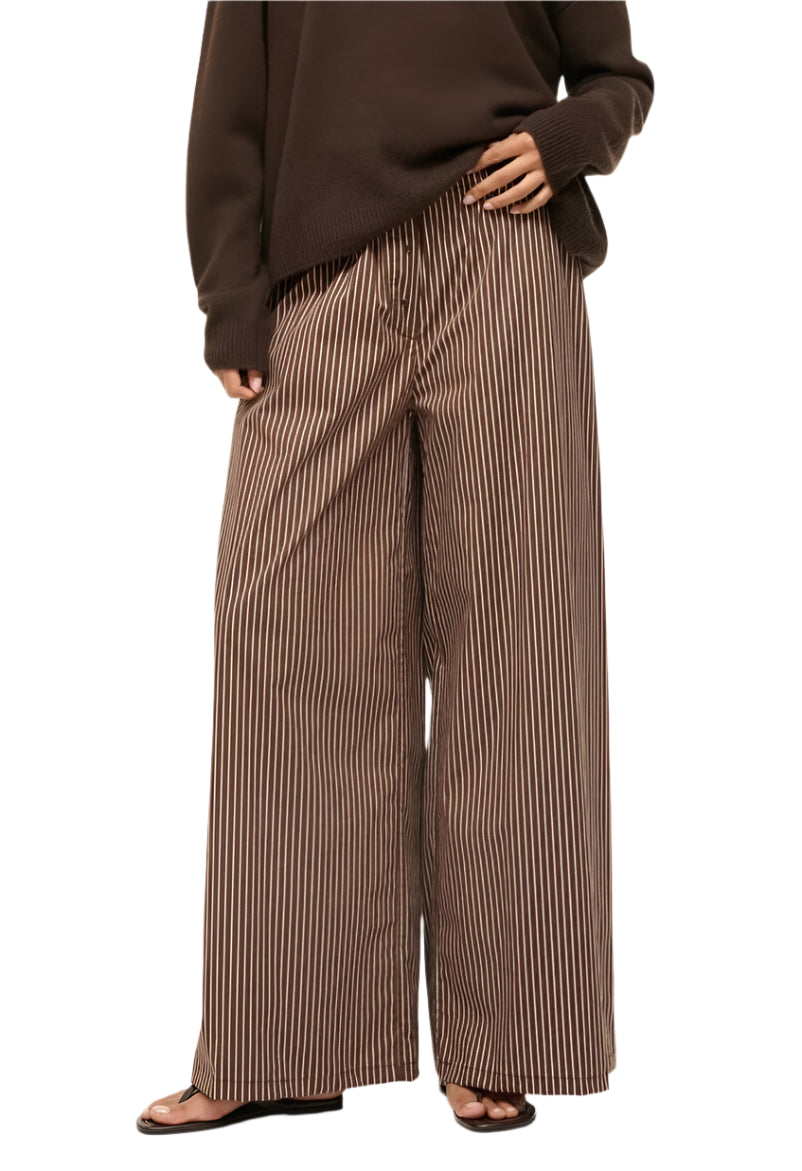 Someone is wearing the Staud Bonfire Pant, featuring loose, wide-leg design and made from cotton poplin, along with a brown sweater while standing with one hand in their pocket.