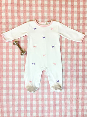 A Baby Girls' Rock Me Romper by The Beaufort Bonnet Company with delicate pink and purple bow embroidery rests on a pink checkered blanket beside a silver rattle.