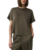 A person wearing the Simkhai Addy Satin T-Shirt, an olive green short-sleeve top with a classic round neckline, paired with matching high-waisted pants, stands with one hand in their pocket against a plain background. The relaxed fit of the ensemble lends effortless style and comfort.