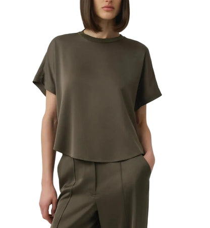 A person wearing the Simkhai Addy Satin T-Shirt, an olive green short-sleeve top with a classic round neckline, paired with matching high-waisted pants, stands with one hand in their pocket against a plain background. The relaxed fit of the ensemble lends effortless style and comfort.