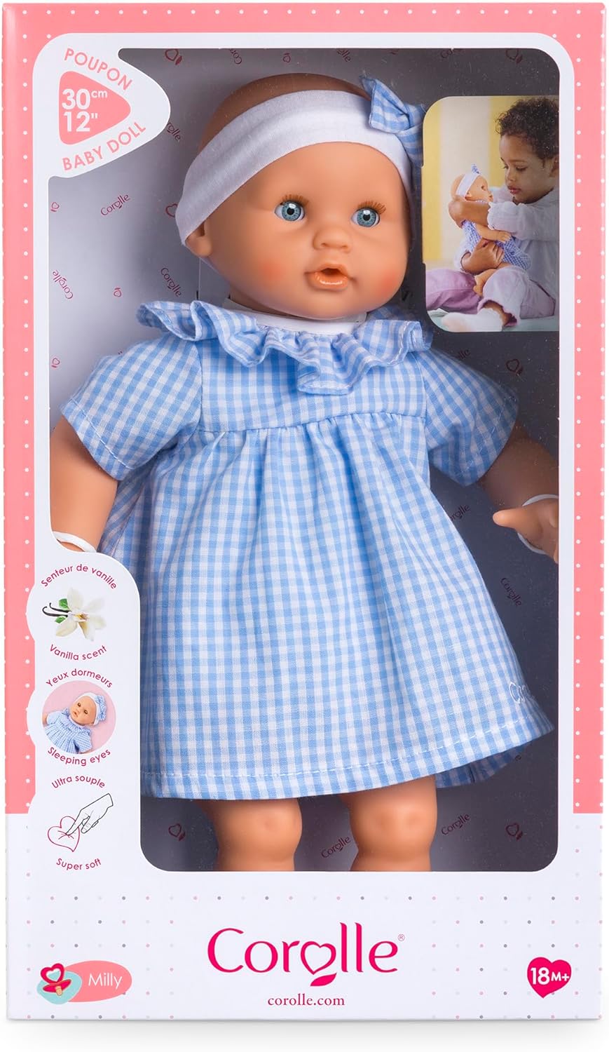 The Corolle Premier Calin - Milly Doll is a soft-bodied baby doll dressed in a blue gingham dress and white headband, displayed in its box featuring product details and a child holding the doll.