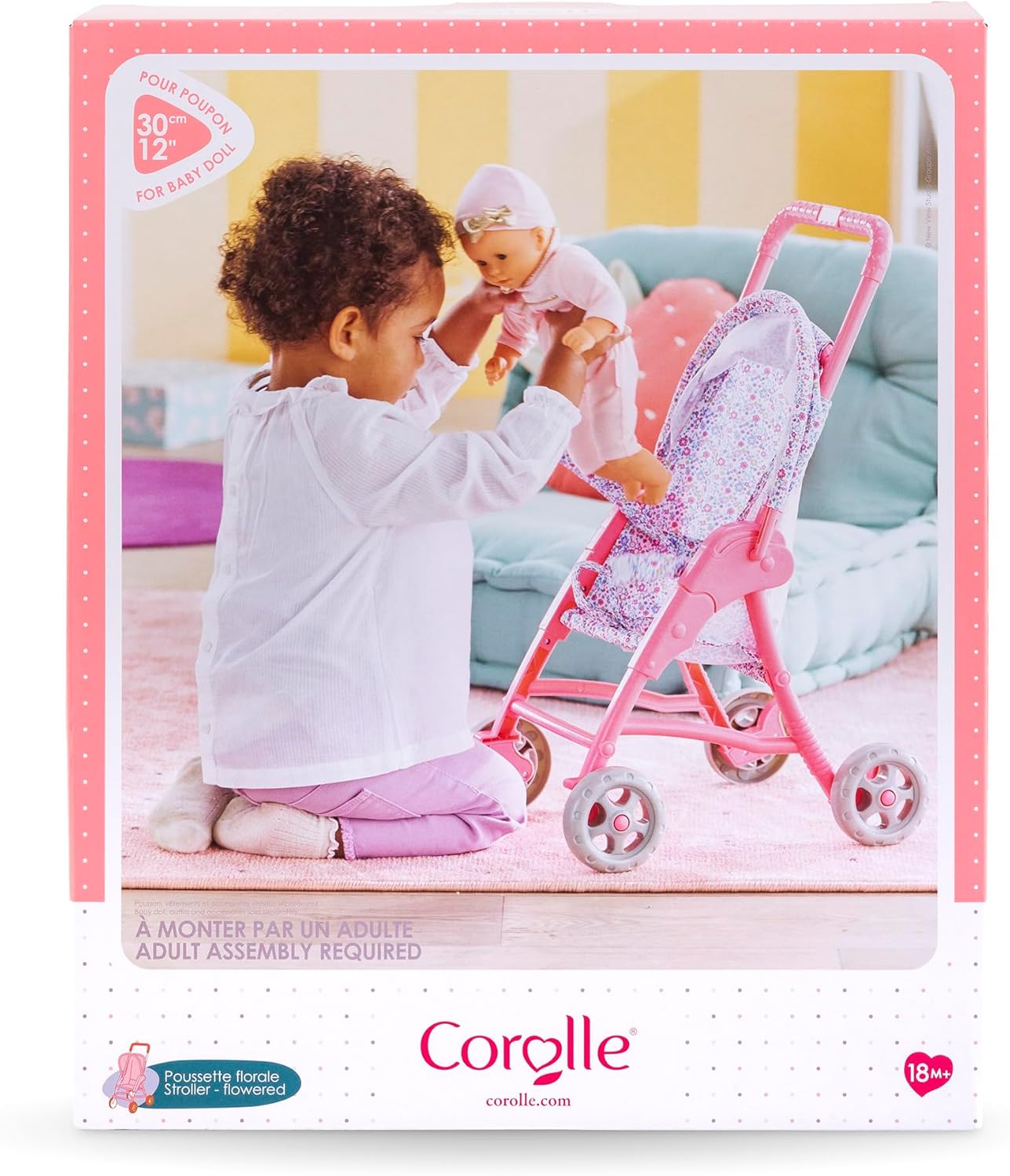 A toddler plays on the floor with a Corolle My First Doll and the Corolle Stroller - Flowered in a cozy living room setting.