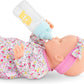 A baby doll wearing a floral outfit and pink headband is lying down, holding the Corolle Magic Milk Baby Doll Bottle for 14-17" to its mouth—the perfect feeding accessory.