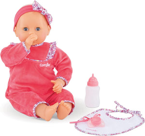 The Corolle Lila Chérie 17" baby doll wears a pink outfit and headband, sits with its thumb in its mouth next to a white bottle and matching pink bib.