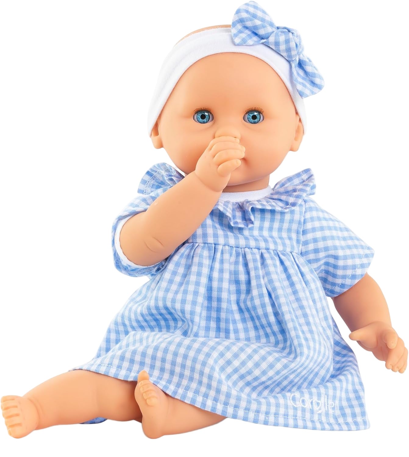 The Corolle Premier Calin - Milly Doll is a soft-bodied baby doll with blue eyes, a white headband with a bow, and a blue and white checkered dress, sitting with its thumb in its mouth.