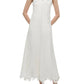 A woman wearing the Simkhai Ellery Bustier Midi Dress—sleeveless with thin straps, subtle leaf patterns, and an uneven hem—paired with white sandals.