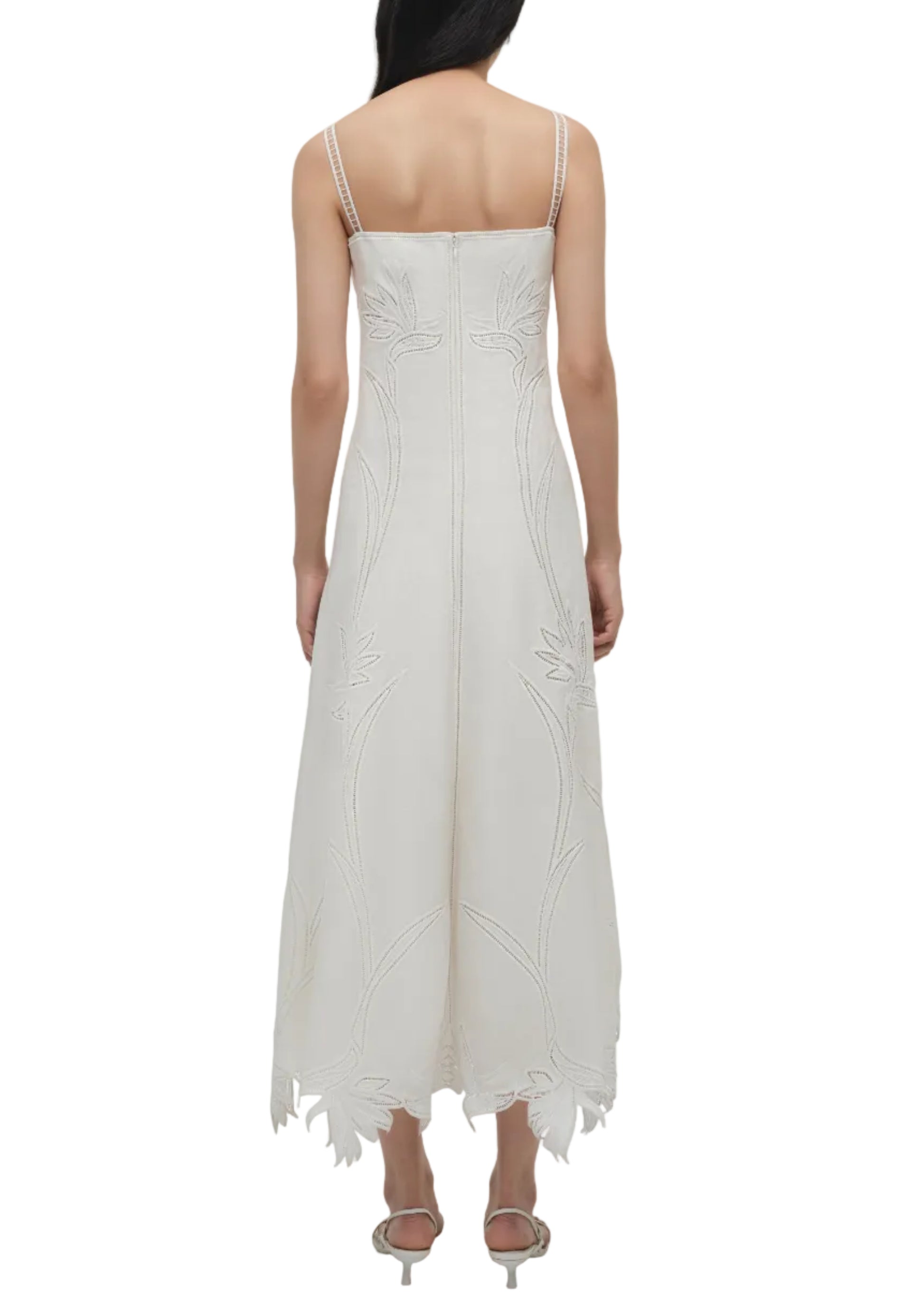 A woman, seen from the back, wears the Simkhai Ellery Bustier Midi Dress—a sleeveless white broderie anglaise dress with thin straps—paired with open-toe heels.