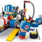 Two LEGO figures in blue helmets work on the LEGO® Super Mario™ Mario Kart™ – Toad's Garage by Legos - Toyhouse, with car parts, tools, and accessories scattered around them on a white background.