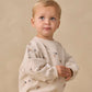 A toddler with short blond hair wears the Quincy Mae Baby Boys’ and Boys’ Oversized Crew Sweatshirt, a cozy fleece pullover adorned with small star and planet prints, standing against a plain beige background—the perfect layering piece for cool days.