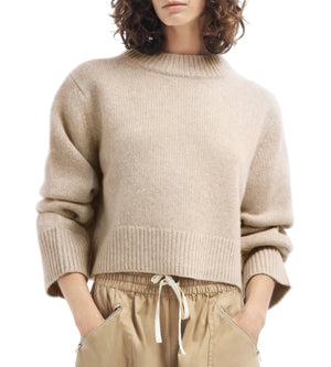 A person wears a CO Cropped Oversized Cashmere Sweater in beige with ribbed cuffs and hem, paired with tan drawstring pants featuring zippered pockets.