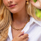 A woman in a white shirt wears Juliska Capucine De Wulf's Berry & Bead Chain necklace and matching earrings, her hand gently touching her earring and collar.