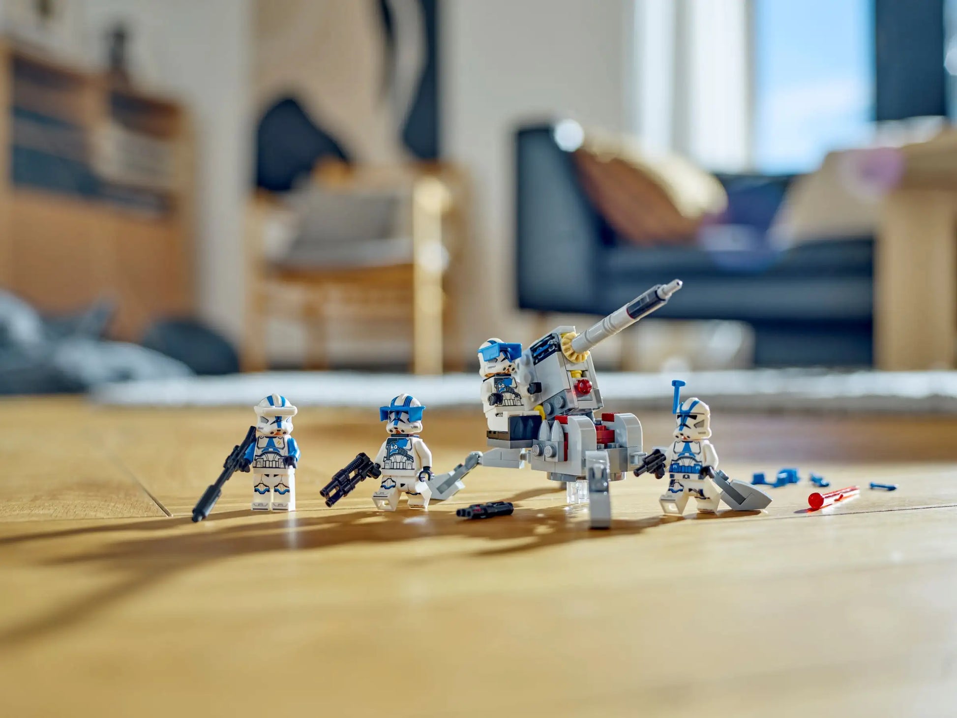 Four minifigures from the LEGO® Star Wars™ 501st Clone Troopers™ Battle Pack by Legos - Toyhouse, each with weapons and an AV-7 anti-vehicle cannon, are displayed on a wooden floor in a bright room.