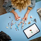 Someone builds the LEGO® Star Wars™ Luke Skywalker™ X-Wing™ Mech from Legos - Toyhouse on a blue table, using various parts, while following instructions displayed on a nearby tablet.