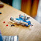 A LEGO® Star Wars™ Captain Rex™ Y-Wing™ Microfighter by Legos - Toyhouse features a Captain Rex minifigure seated on a blue and white Microfighter with two red LEGO pieces and a blaster displayed on a wooden table.