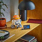 The LEGO® Star Wars™ Chopper (C1-10P)™ Astromech Droid by Legos - Toyhouse is displayed with a small plaque on a wooden shelf beside a potted plant, lamp, and books—an ideal collectible for any Star Wars Ahsoka fan.