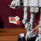 A hand displays a small speeder set beside the larger LEGO® Star Wars™ AT-AT™ model by Legos - Toyhouse on a wooden table.