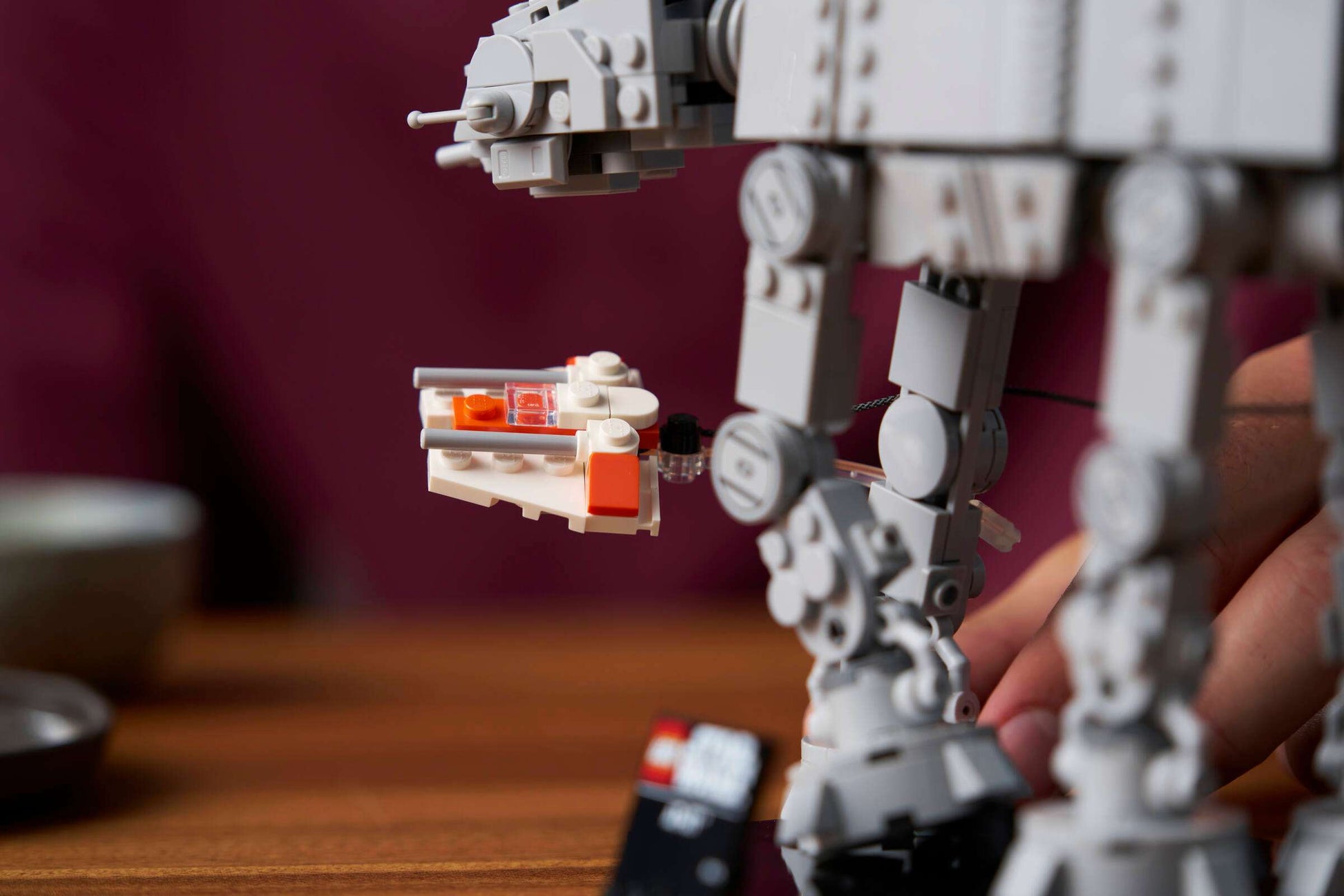 A hand displays a small speeder set beside the larger LEGO® Star Wars™ AT-AT™ model by Legos - Toyhouse on a wooden table.