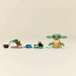 The Legos - Toyhouse LEGO® Star Wars™ Grogu's Homestead set features a Grogu figurine beside accessories like a plant and frog, recreating a charming homestead scene against a simple background.
