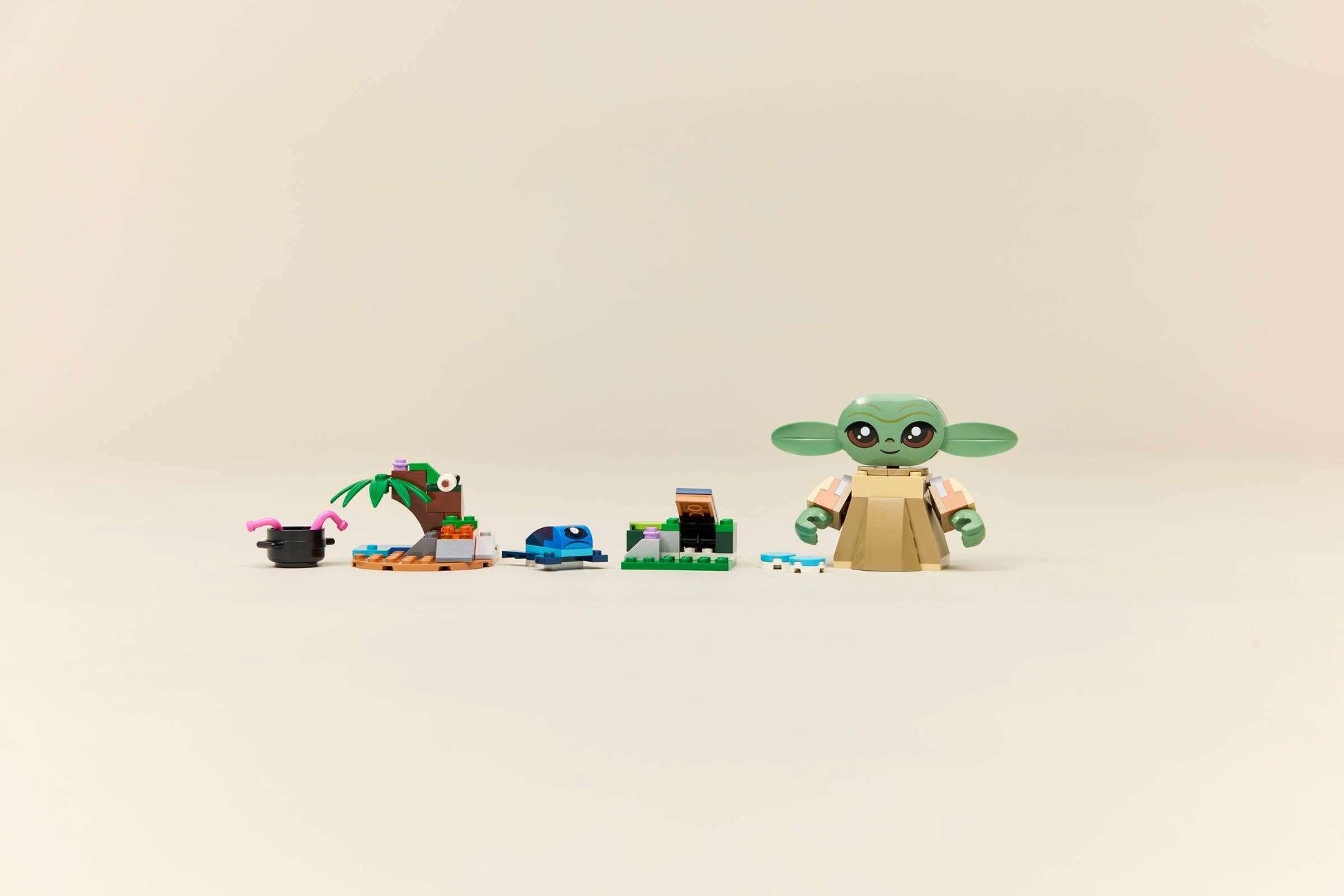 The Legos - Toyhouse LEGO® Star Wars™ Grogu's Homestead set features a Grogu figurine beside accessories like a plant and frog, recreating a charming homestead scene against a simple background.