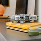 A Legos - Toyhouse LEGO® Star Wars™ Anzellan Starship model rests on yellow books on a gray cabinet, with nearby headphones, a Grogu toy, various objects, and insect illustrations in the background.
