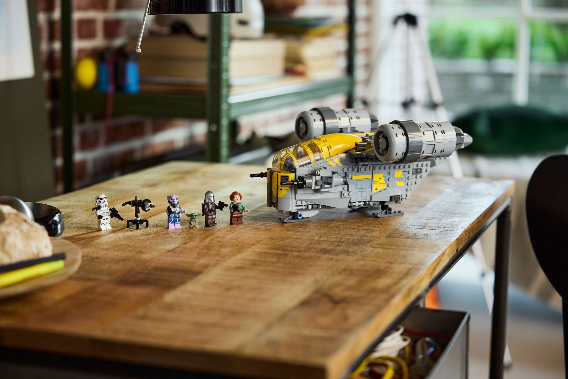 The Legos - Toyhouse LEGO® Star Wars™ The Razor Crest™ set and six minifigures are displayed on a wooden table in a bright room with shelves and a window in the background.