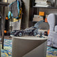 The LEGO® DC Batman Forever™ Batmobile™ and Batman minifigure by Legos - Toyhouse are displayed on a round table in a room with a skateboard, chair, books, and a backpack—ideal for LEGO DC Batman fans.
