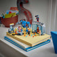 LEGO® Marvel Iron Man's Laboratory: Hall of Armor by Legos - Toyhouse, featuring Iron Man minifigures and accessories, is displayed atop two stacked books on a windowsill with other desk items in the background.