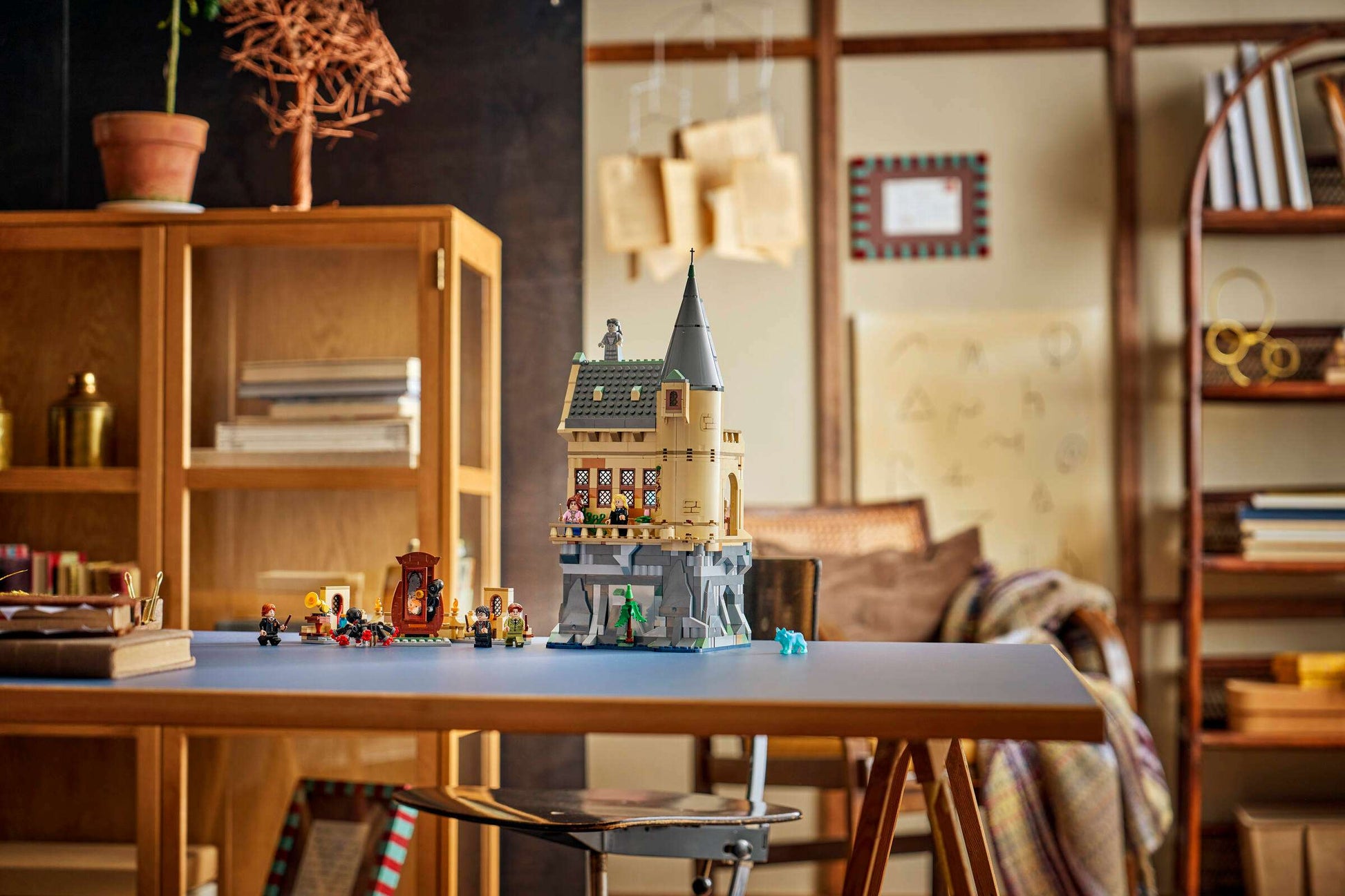 A LEGO® Harry Potter™ Hogwarts™ Castle: Hospital Wing set by Legos - Toyhouse is displayed on a table in a cozy room with wooden shelves filled with books and decorative items in the background.