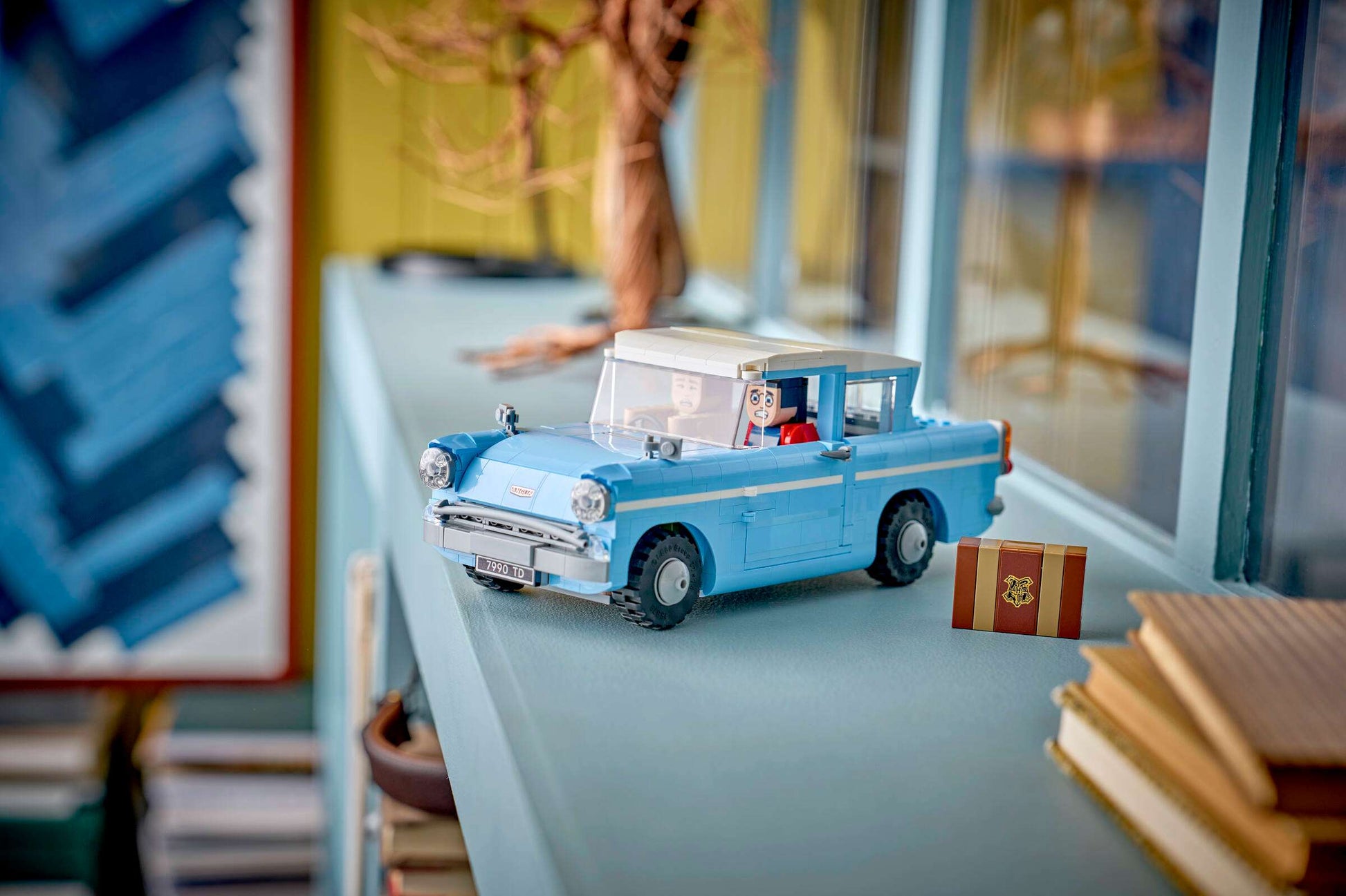 The LEGO® Harry Potter™ Enchanted Flying Ford Anglia™ by Legos - Toyhouse, along with a small brown box, is displayed on a light blue shelf near books and a window.