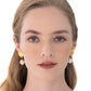 A woman with fair skin and light brown hair wears Jennifer Behr Alana Earrings, showcasing golden scallop shells and baroque pearls against a white background.