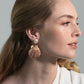 Woman with light brown hair wears Jennifer Behr's Folly Earrings, crafted from natural seashells, and a white top, shown in profile against a neutral background.