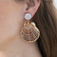 A close-up of a woman's ear wearing Jennifer Behr's Folly Earrings, which feature a white pearl stud with a large natural seashell dangling below.