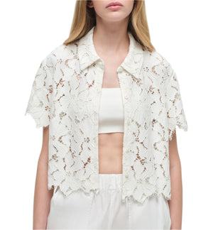 A woman wears the Simkhai Marjorie Camp Shirt, a short-sleeved, floral lace button-up, over a white bandeau top with white pants for a feminine look.