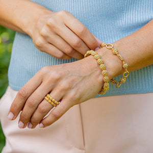 A person wearing a gold ring, the Juliska Capucine De Wulf Berry & Bead Bracelet, and a twisted chain bracelet, with hands resting on a light blue top and light pink pants.