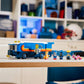 The LEGO® Sonic the Hedgehog™ Team Sonic Command Truck by Legos - Toyhouse features a blue and orange gaming truck and five character figures, shown on a desk in a room with shelves in the background.