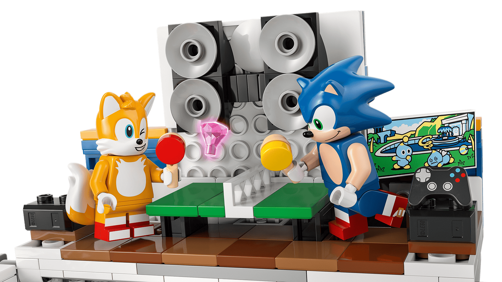 Two LEGO® Sonic the Hedgehog™ Team Sonic Command Truck figures—Tails and Sonic—play table tennis near a speaker wall, with a TV, game controller, and a Sonic toy on a side table. Brand: Legos - Toyhouse.