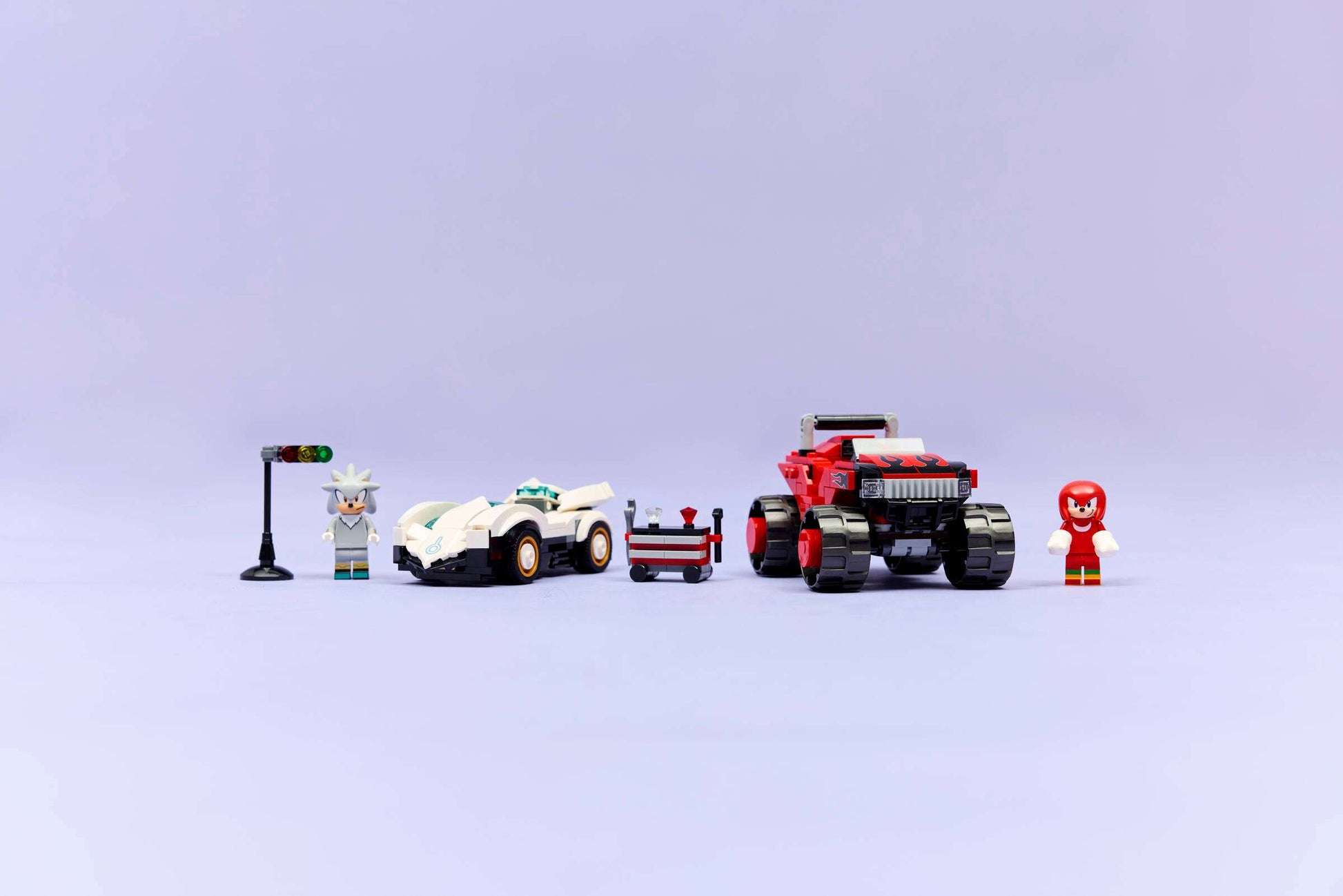 The LEGO® Sonic the Hedgehog™ Silver's Car vs. Knuckles' Monster Truck set by Legos - Toyhouse includes two cars, a traffic light, cart, and two minifigures—perfect for fans of video game building toys on a light purple background.