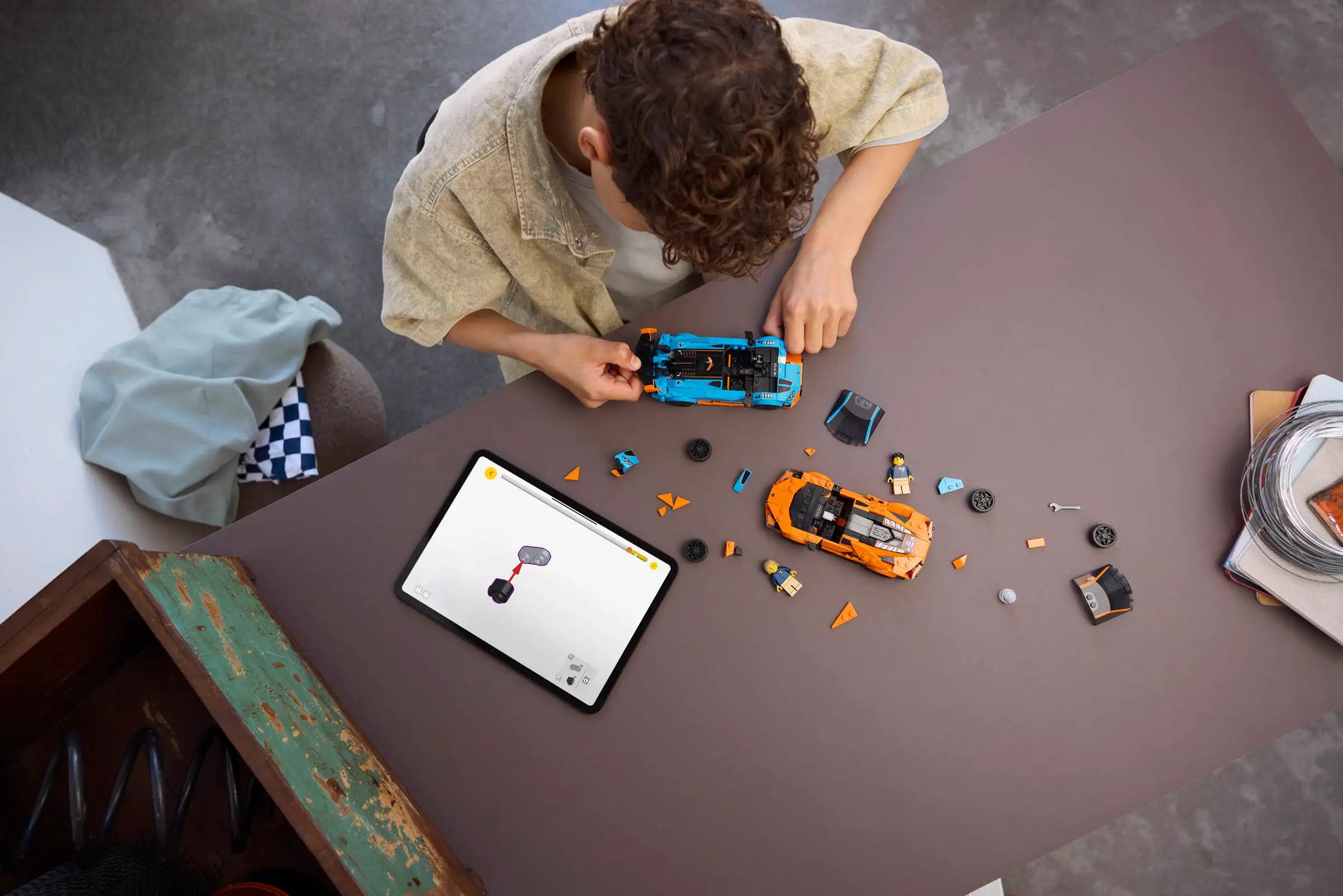 Someone assembles Legos - Toyhouse LEGO® Speed Champions Lamborghini Revuelto & Huracán STO sets with small parts on a table, following instructions displayed on an open tablet nearby.