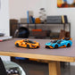 Two LEGO® Speed Champions Lamborghini Revuelto & Huracán STO cars—orange and blue by Legos - Toyhouse—are displayed on a wooden desk in a modern, organized room with shelves and books, ideal for car-building fans.