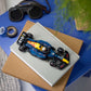A LEGO® Speed Champions Oracle Red Bull Racing RB20 F1® Race Car by Legos - Toyhouse sits atop two closed books on a blue table, next to goggles, tape, and a green plant.