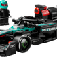 The LEGO® Speed Champions Mercedes-AMG F1® W15 Race Car by Legos - Toyhouse includes a race car model and a minifigure with a black racing suit and turquoise helmet standing beside it.