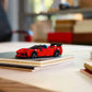 A LEGO® Speed Champions Ferrari SF90 XX Stradale Sports Car by Legos - Toyhouse is displayed on a closed notebook atop a light-colored desk, surrounded by office supplies and blurred shelves in the background.