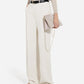 A person wears CO Tailored Straight Leg Trousers in white, a beige long-sleeve top, black belt, beige sandals, and holds a beige chain-strap clutch.