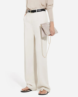 A person wears CO Tailored Straight Leg Trousers in white, a beige long-sleeve top, black belt, beige sandals, and holds a beige chain-strap clutch.