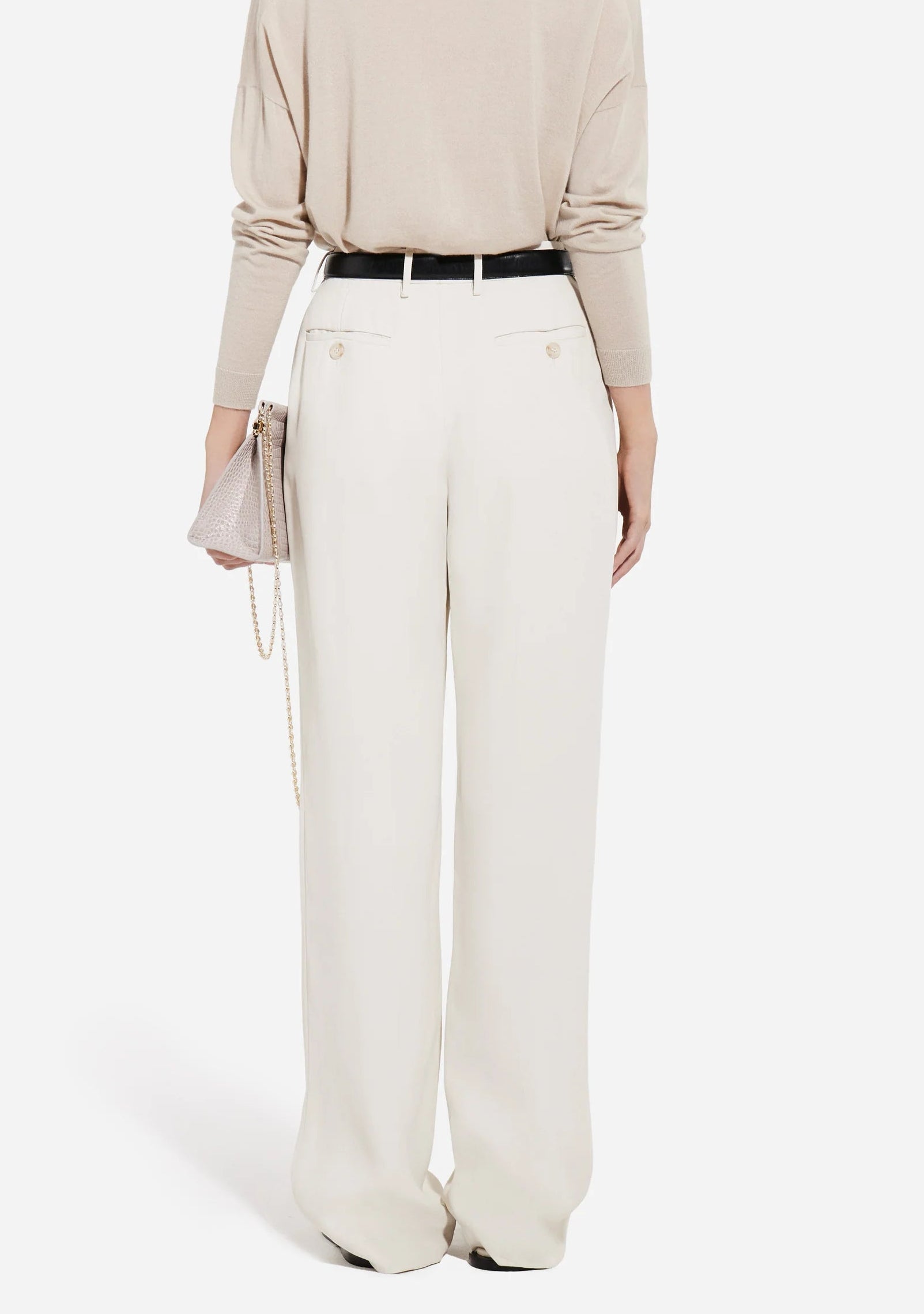 Person facing away from the camera, wearing a beige top, CO Tailored Straight Leg Trouser in white, a black belt, and holding a small light pink chain-strap bag.
