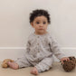 A baby wearing the Quincy Mae Baby Boys’ Waffle Long Sleeve Jumpsuit sits on the floor holding a pine cone, with a wooden toy beside them.