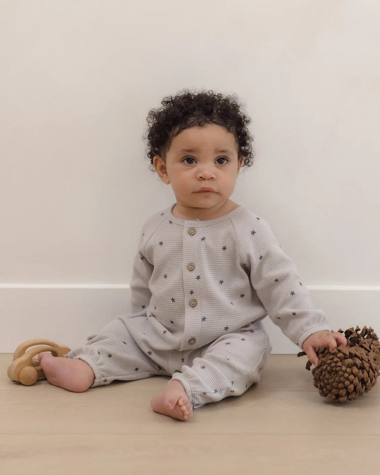 A baby wearing the Quincy Mae Baby Boys’ Waffle Long Sleeve Jumpsuit sits on the floor holding a pine cone, with a wooden toy beside them.